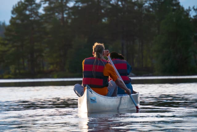 Two people are paddling a canoe on a calm lake while wearing life jackets.