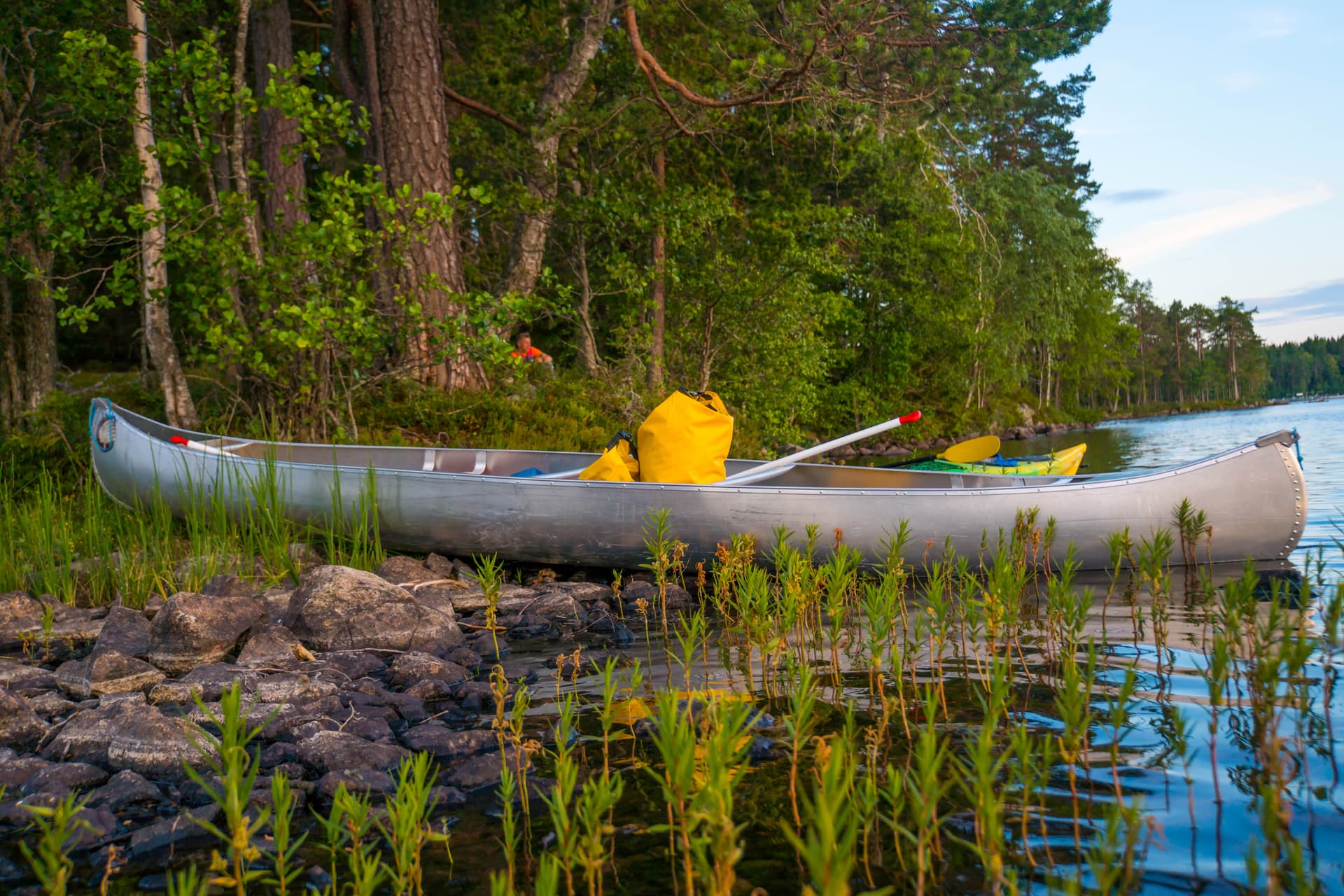 A canoe on land with a paddle, life jacket and a waterproof bag.