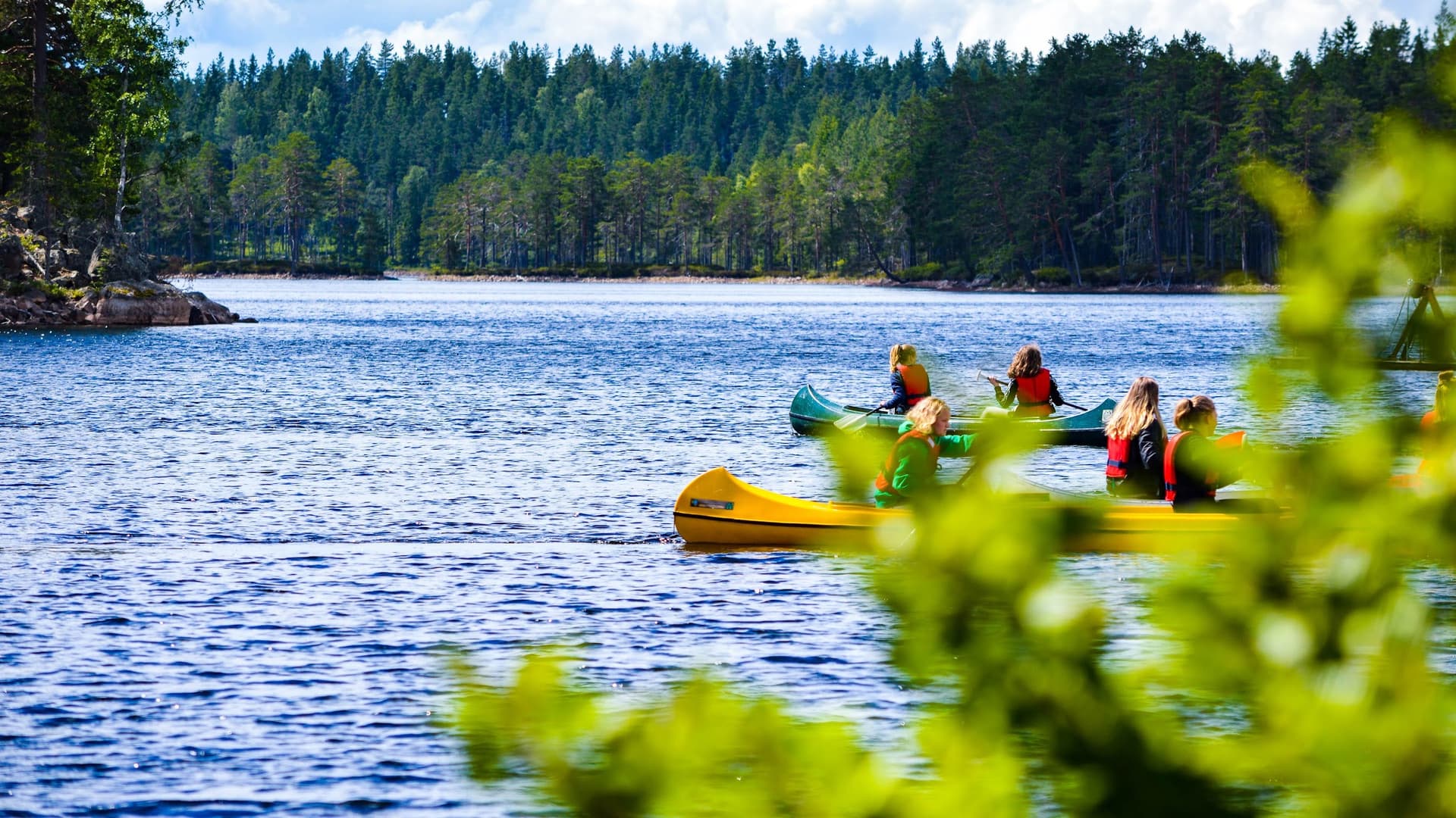 A group of teens canoeing in the Malingsbo-Kloten Nature Reserve, surrounded by lush green nature.