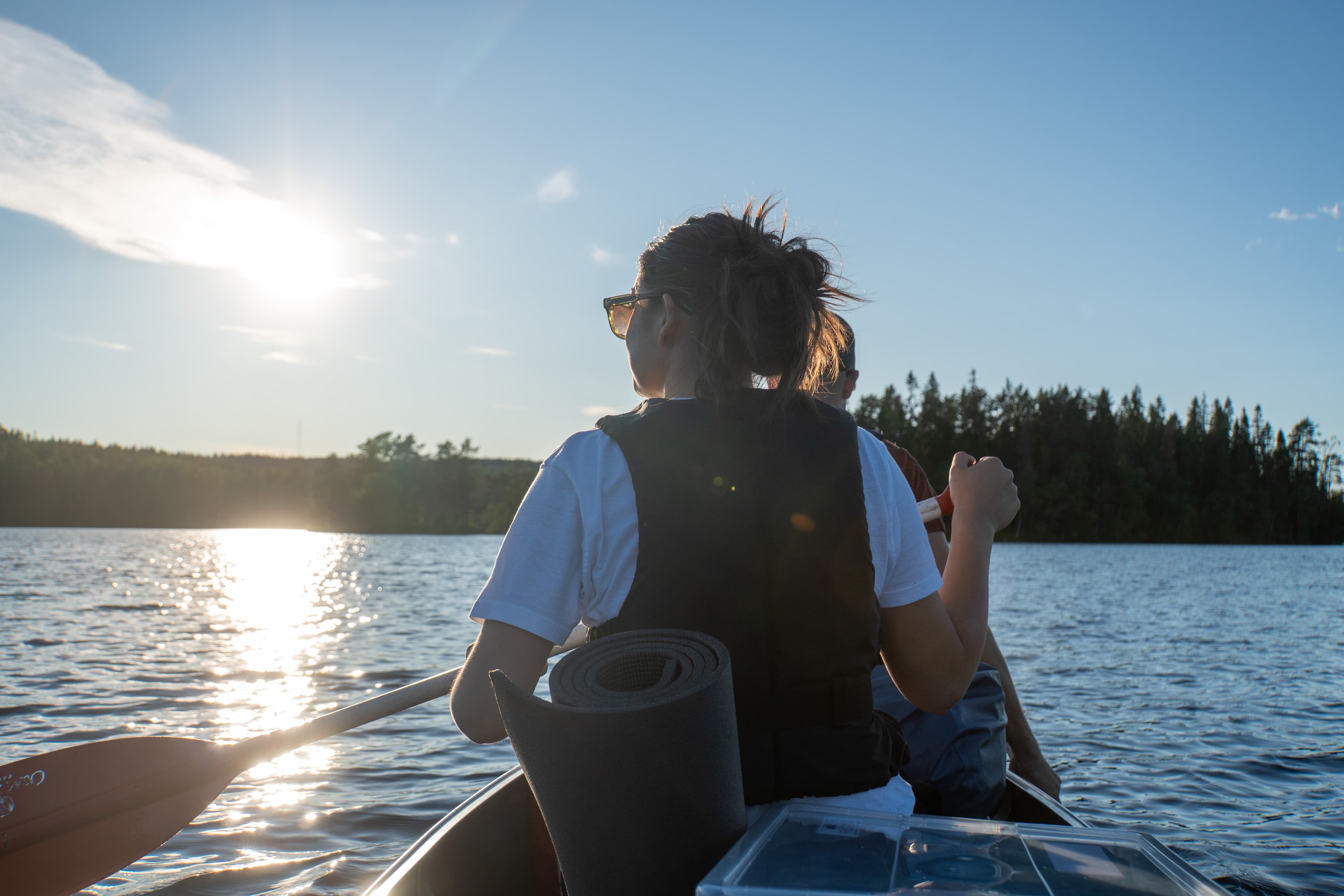 A joung woman wearing sunglasses while soaking in the sun on a canoe trip.