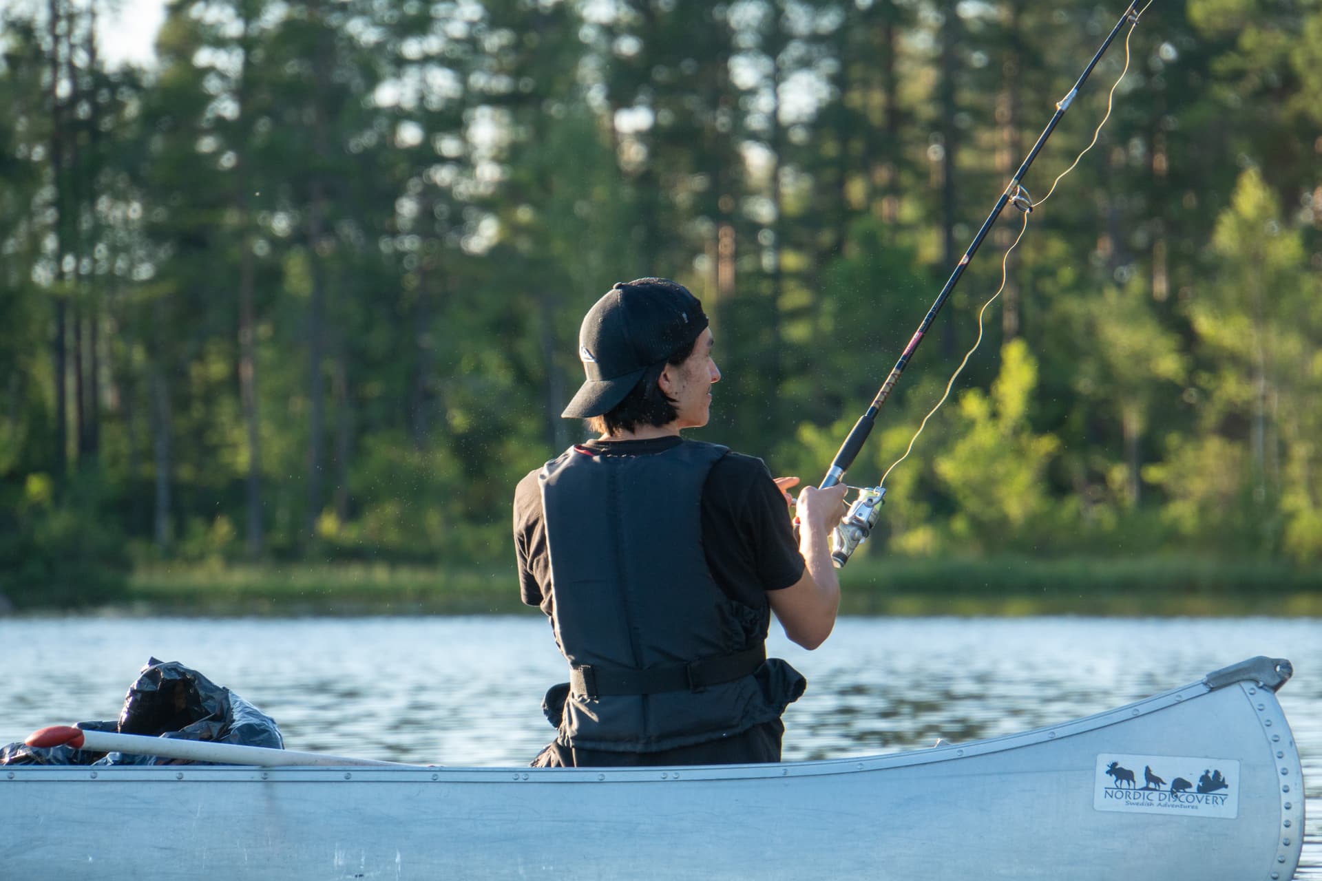 Un ragazzo seduto in una canoa pronto a lanciare la sua lenza nell'acqua.