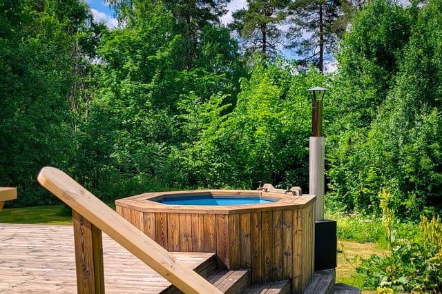 Wood-heated hot tub in the sunshine surrounded by green trees.