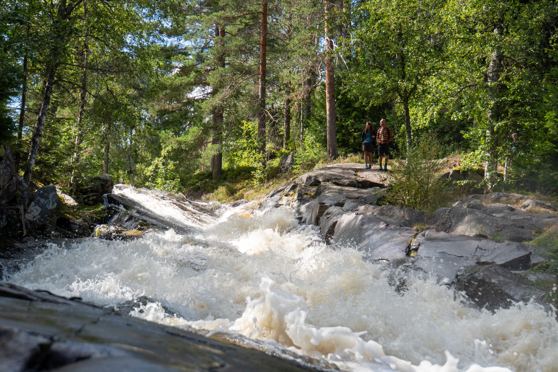 Un couple se tenant devant la cascade de skräddartorpsfallet lors d’une randonnée dans la réserve naturelle de Malingsbo-Kloten en Suède.