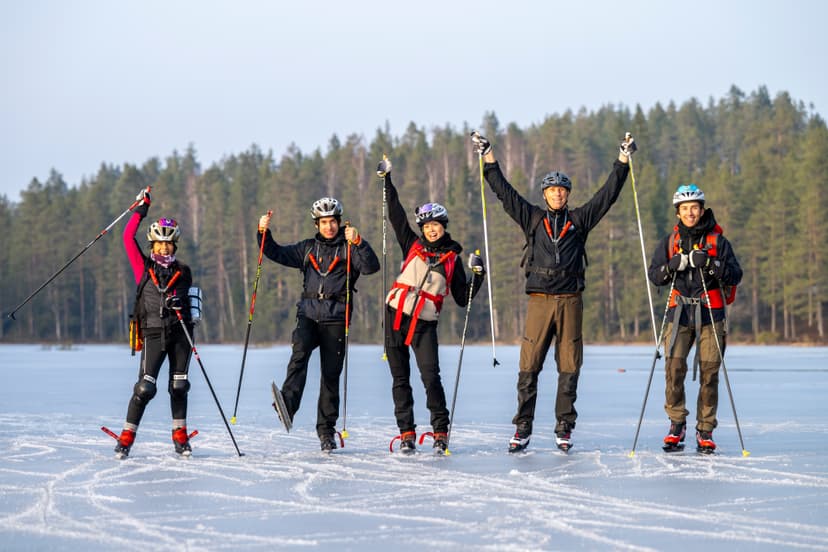 Cinq personnes sur un lac gelé avec casques et patins, tenant des bâtons et célébrant devant une forêt.