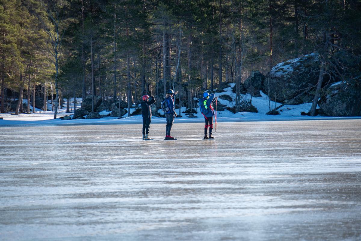 Tres participantes de la excursión de patinaje sobre hielo mirando algo en la distancia en un lago congelado en la naturaleza sueca.
