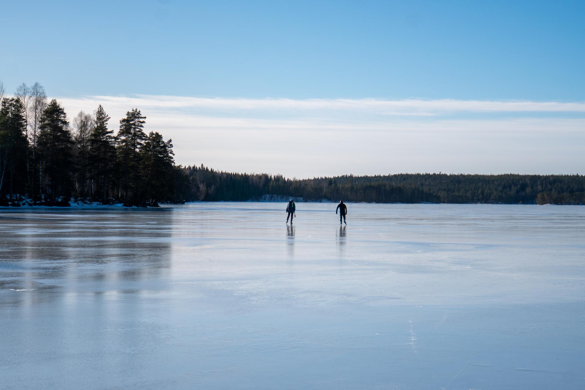 Una pareja de patinadores en la distancia disfruta del cielo despejado y el hielo liso durante una excursión de patinaje sobre hielo guiada.