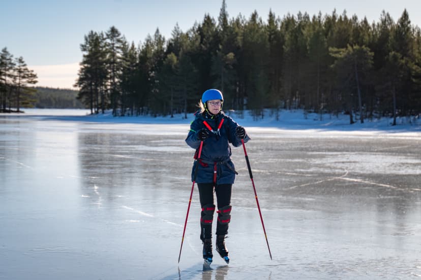 Eine glückliche Frau, die auf einem gefrorenen See in der schwedischen Wildnis Schlittschuh läuft.