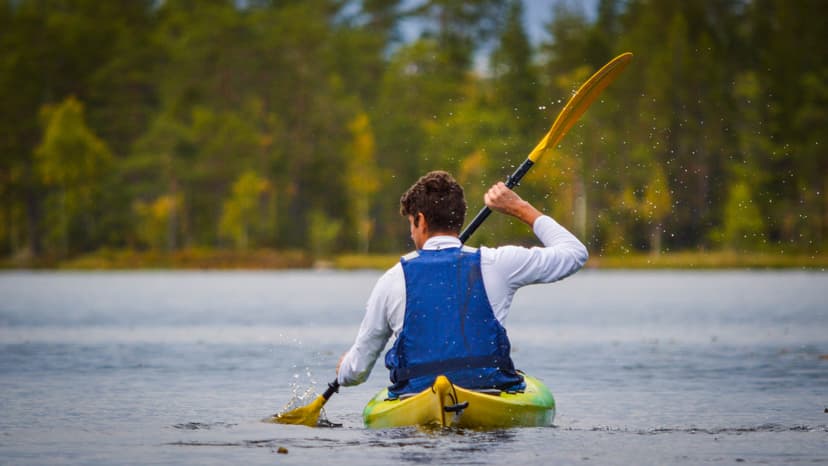 Un jeune homme en voyage en kayak pagayant pour que l'eau éclabousse derrière lui.