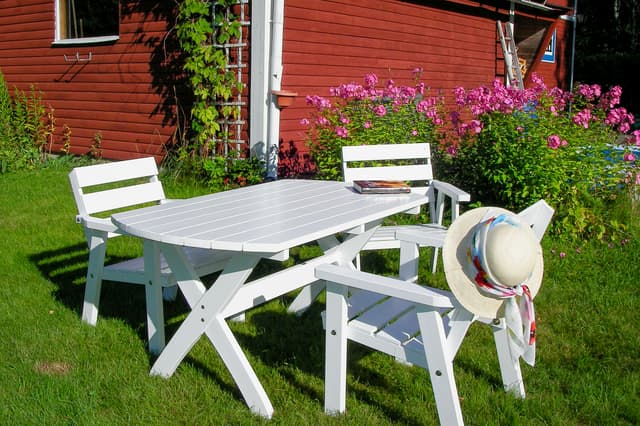 Tre vita trädgårdsstolar i trädgården på wilderness lodge i Sverige. En bok och solhatt på en av stolarna.