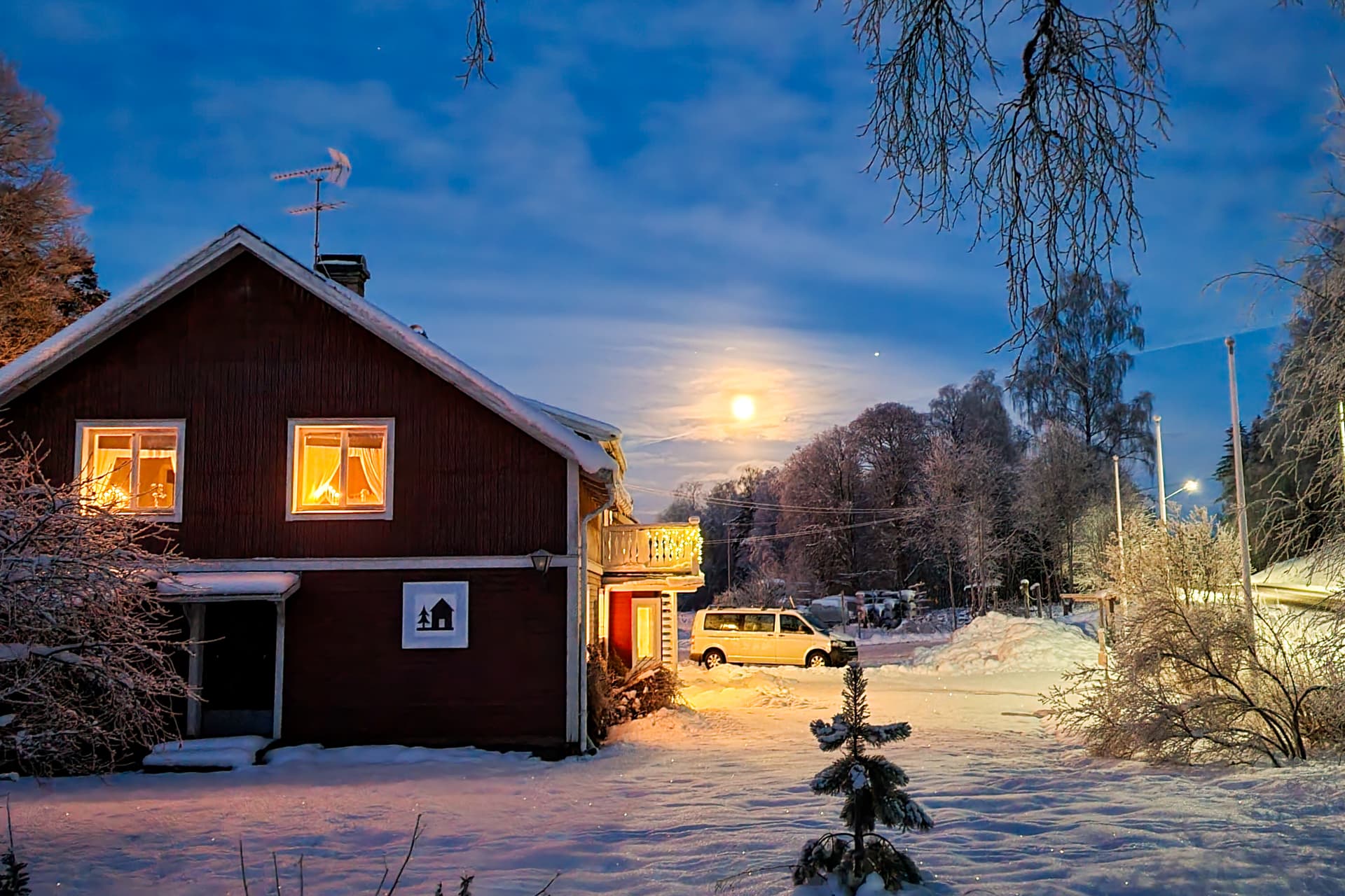 The Wilderness Lodge in Sweden at night with the lights on. The moon is shining in the sky.