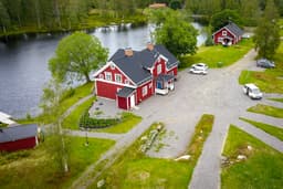 A bird's eye view of the River Lodge with the lake in the background and the camping area in the foreground. The sauna, swimming area, and deck are visible from above.