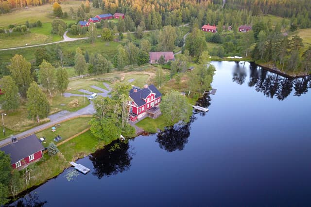 En översikt över flodstugans egendom och campingområdet. Sjön, den gröna gräsmattan för att slå upp tält och bastun syns ovanifrån.
