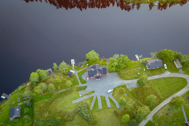 Flygbild av River Camping. Vattnet är lugnt och campingområdet omges av vildmark.