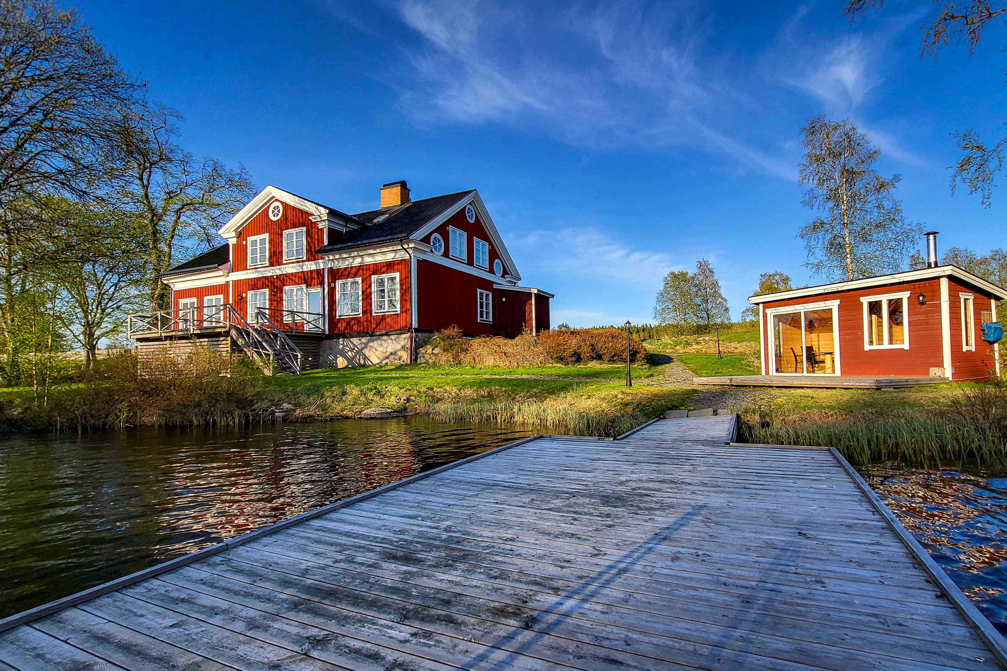 Däcket vid River Camping med utsikt över bastun och sittgruppen. River Lodge syns i bakgrunden.