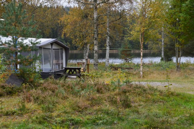 En husvagn och en bänk på vildmarkscampingen intill vattnet.