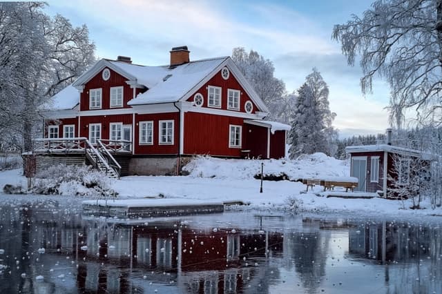 Flodstugan ligger mitt i en snöig vinterlandskap med is på sjön och snö på träden.