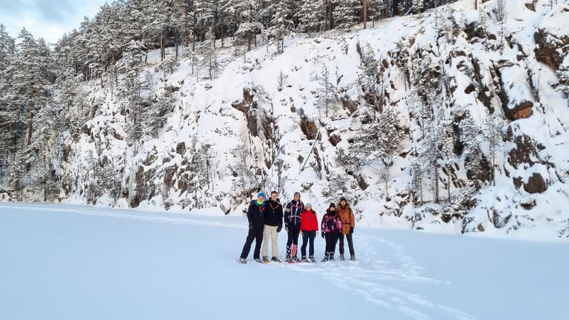 Die Gruppe macht eine Pause vor Klippen auf einem gefrorenen See während einer geführten Wolfsspürungstour von Nordic Discovery.